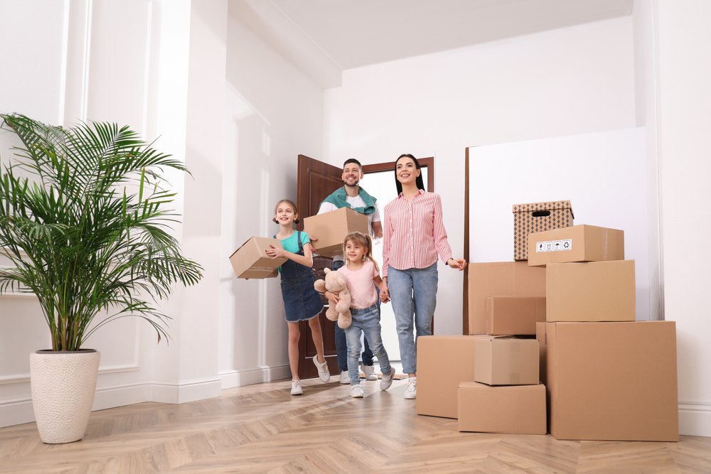 Two parents and children standing in a room around moving boxes during a family move.